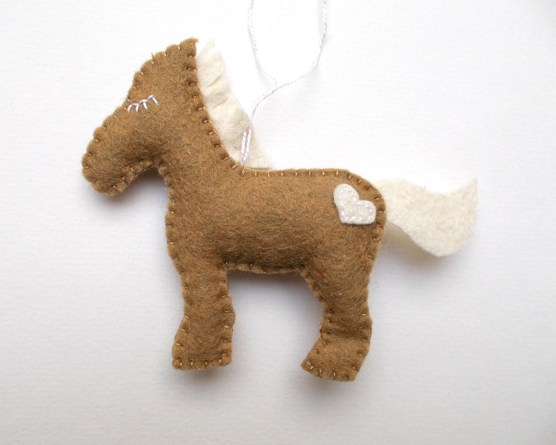 May include: A brown felt horse ornament with a white felt mane and tail. The horse has a white felt heart on its side.