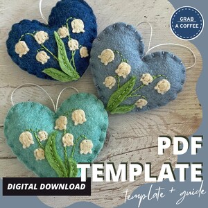 Puede incluir: Tres adornos de fieltro en forma de coraz&oacute;n en tonos azules y turquesas, cada uno adornado con flores de lirios de los valles bordadas. Los adornos tienen cuerdas blancas para colgar. El texto en la imagen dice "PDF TEMPLATE" y "DESCARGA DIGITAL".