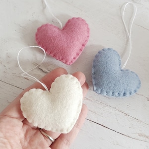Peut inclure: Trois décorations en forme de cœur en feutre rose, bleu et blanc. Chaque cœur est doté d'une ficelle blanche pour l'accrocher.