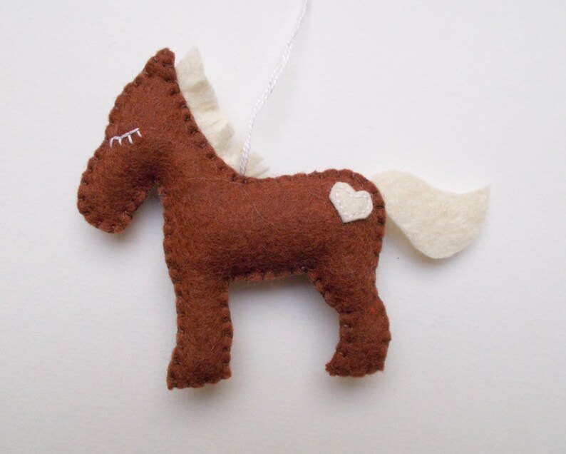 May include: A brown felt horse ornament with a white felt mane, tail, and heart on its back.