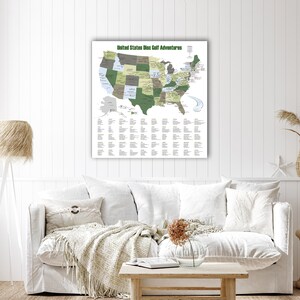 May include: A framed map titled "United States Disc Golf Adventures" hangs on a white wall. The map highlights states in shades of green and gray, with a list of locations below. The room features a white sofa with pillows and a wooden coffee table.