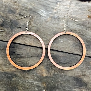 May include: A pair of wooden hoop earrings with a natural wood grain finish. The earrings are a light brown color and have a simple, circular design.