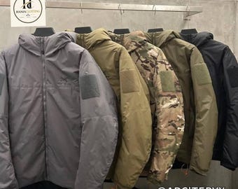 May include: A row of five hooded jackets hanging on a rack, featuring colours including grey, olive green, camouflage, and black. Each jacket has a full-length front zip, a hood, and a rectangular velcro patch on the upper sleeve area.