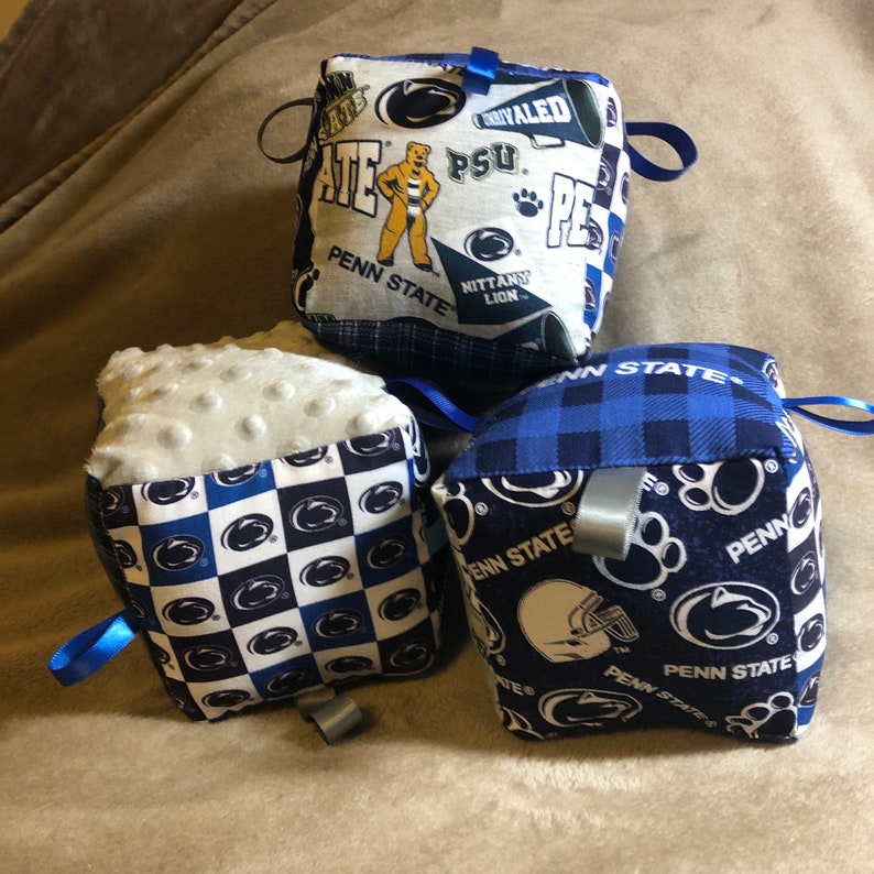 May include: Three blue and white fabric cubes with different Penn State University designs. The cubes have a soft, textured surface and are perfect for babies and toddlers.