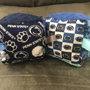 May include: Two blue and white Penn State Nittany Lions themed throw pillows. One pillow has a checkered pattern with the Nittany Lion logo. The other pillow has a blue background with the Nittany Lion logo, paw prints, and the words "Penn State".