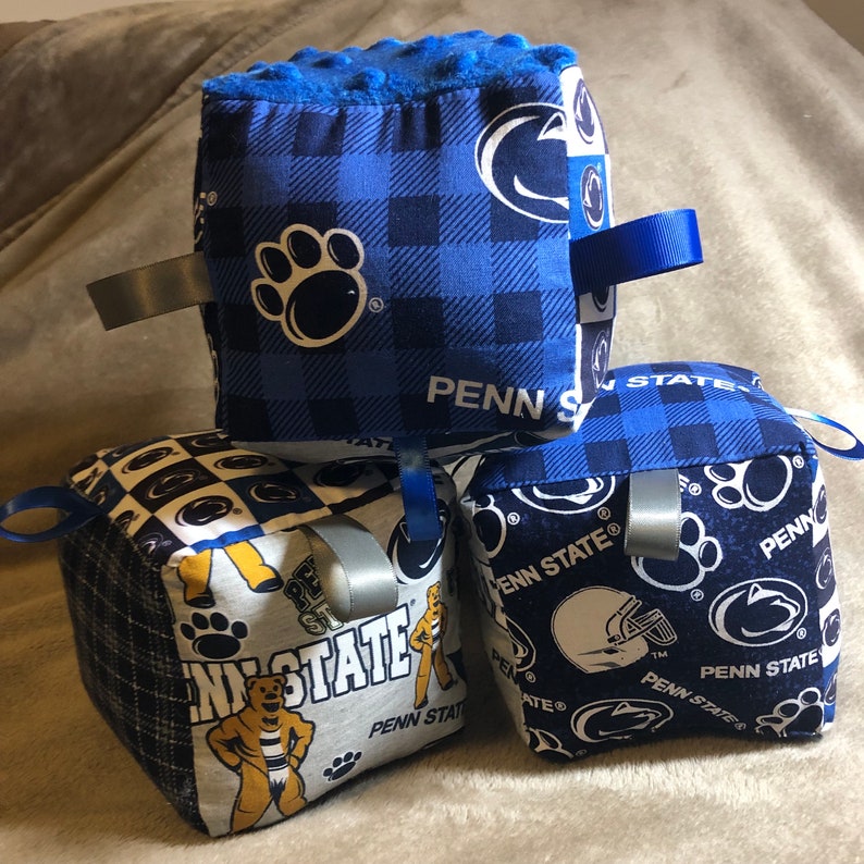 May include: Three blue and white fabric cubes with different Penn State logos and designs. The cubes are made of soft fabric and have a variety of textures. They are perfect for babies and toddlers to play with and explore.
