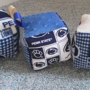 May include: Three blue and white fabric cubes with different patterns. One cube has a blue and white checkered pattern with the text "Penn State" and "Nittany Lions". Another cube has a blue and white checkered pattern with the text "Penn State". The third cube has a blue and white polka dot pattern with the text "Penn State".