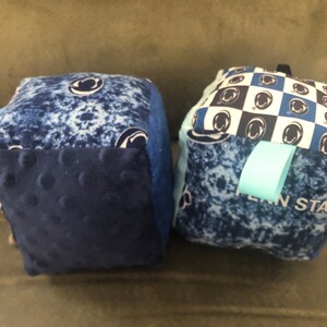 May include: Two blue and white fabric cubes with a Penn State logo. One cube has a checkered pattern and the other has a blue and white tie-dye pattern.