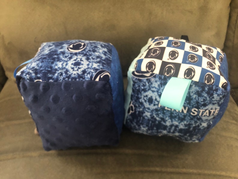 May include: Two blue and white fabric cubes with a Penn State logo. One cube has a checkered pattern and the other has a blue and white tie-dye pattern.