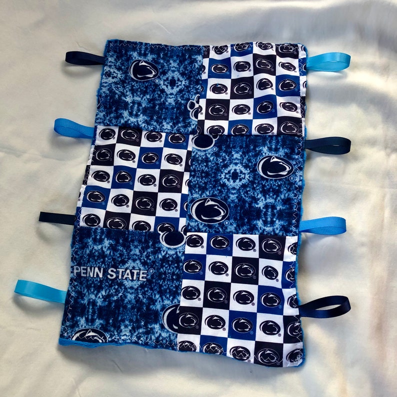 May include: A blue and white baby blanket with a Penn State logo and a checkered pattern. The blanket has blue ribbon ties on each corner.