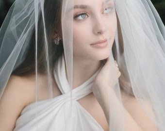May include: A woman wearing a white bridal gown with a white veil covering her face. The veil is sheer and delicate, and the gown has a halter neckline.