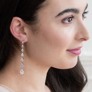 May include: A pair of long, silver dangle earrings with pear-shaped clear crystals. The earrings are approximately 2 inches long.
