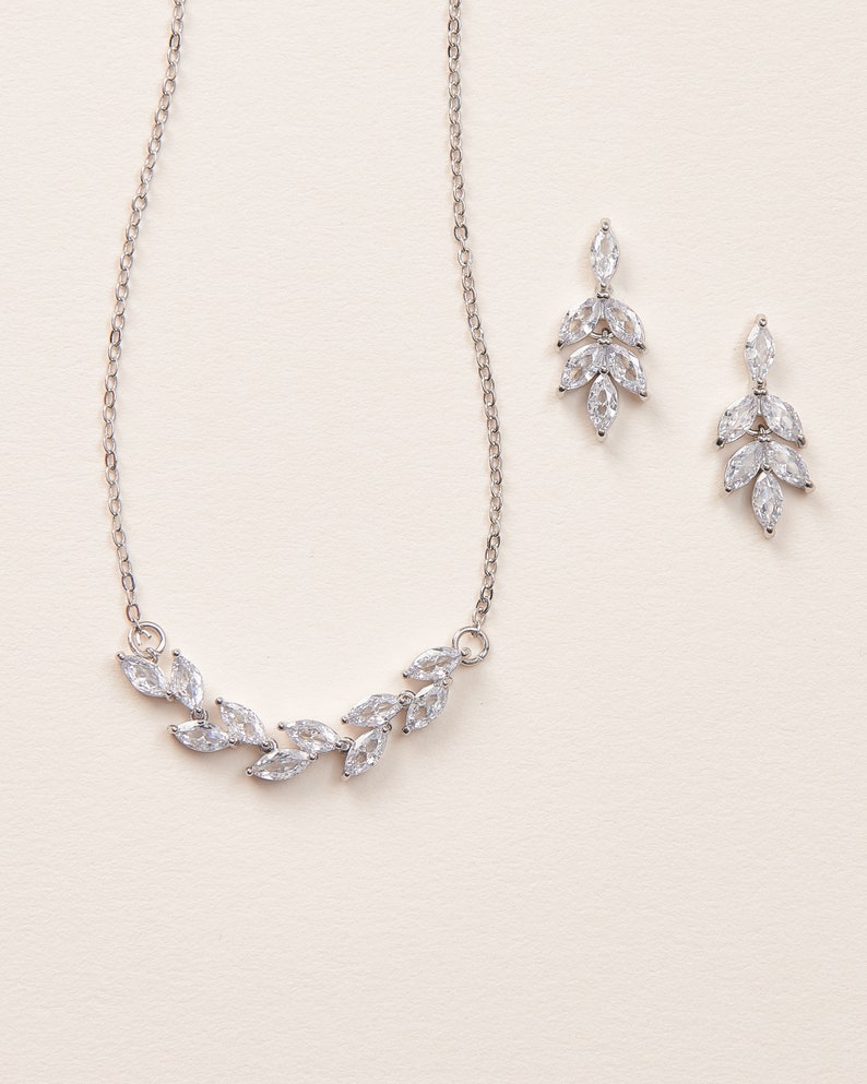 May include: A silver necklace and earrings set with a delicate leaf design featuring clear cubic zirconia stones.