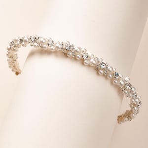 May include: A delicate silver headband adorned with faux pearls and rhinestones. The headband is flexible and can be adjusted to fit most head sizes.