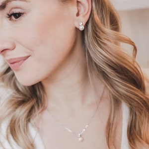 May include: A silver-toned necklace featuring a single white pearl pendant suspended from a delicate chain, paired with matching stud earrings that each consist of a small clear stone set above a round white pearl.