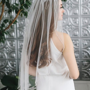 Op de afbeelding: Een eenlaags bruidssluier met een parelrand. De sluier is gemaakt van zacht tule en is perfect voor een eenvoudige en elegante bruiloftlook.