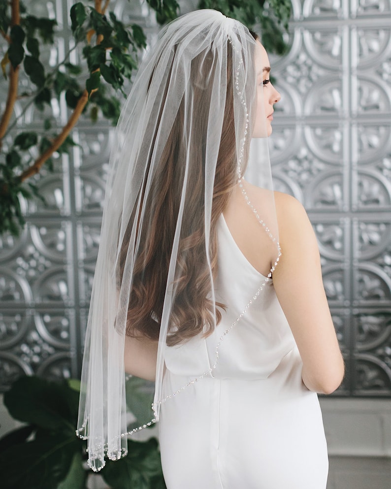 Op de afbeelding: Een eenlaags bruidssluier met een parelrand. De sluier is gemaakt van zacht tule en is perfect voor een eenvoudige en elegante bruiloftlook.