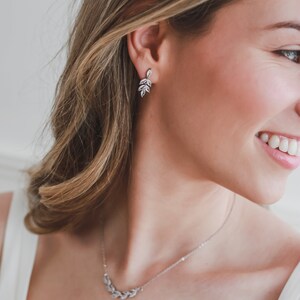 May include: A silver necklace and earrings with a delicate leaf design. The necklace features a curved row of leaves, while the earrings have a dangling cluster of leaves.
