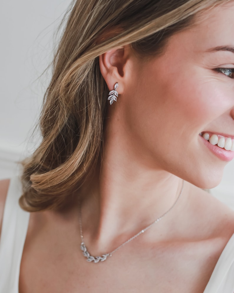May include: A silver necklace and earrings with a delicate leaf design. The necklace features a curved row of leaves, while the earrings have a dangling cluster of leaves.