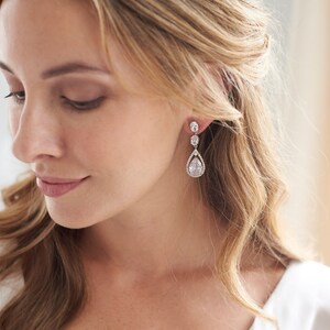 May include: A pair of silver teardrop earrings with clear crystal stones. The earrings have a pear-shaped stone in the center, surrounded by smaller stones.