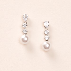 May include: A pair of silver dangle earrings with a pearl and clear crystal accents.