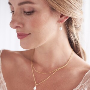 Pu&ograve; includere: Una collana d'oro con un ciondolo a perla singola e orecchini pendenti a perla abbinati. La collana &egrave; composta da due catene sovrapposte.