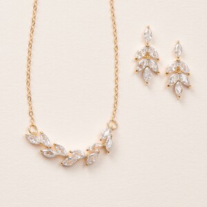 May include: A gold necklace and earrings set with a delicate leaf design featuring clear cubic zirconia stones.