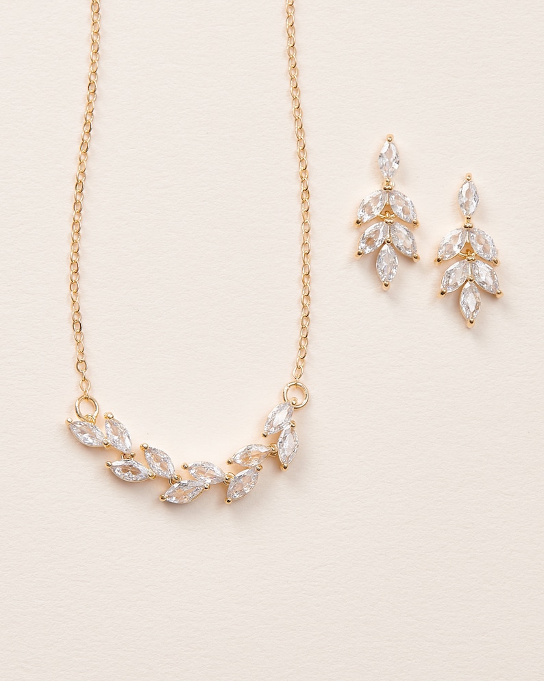 May include: A gold necklace and earrings set with a delicate leaf design featuring clear cubic zirconia stones.