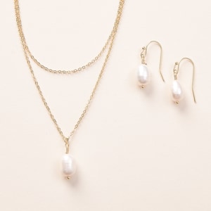 Pu&ograve; includere: Una collana a catena dorata con un ciondolo a perla singola e orecchini a goccia di perla abbinati. La collana &egrave; composta da due catene sovrapposte.