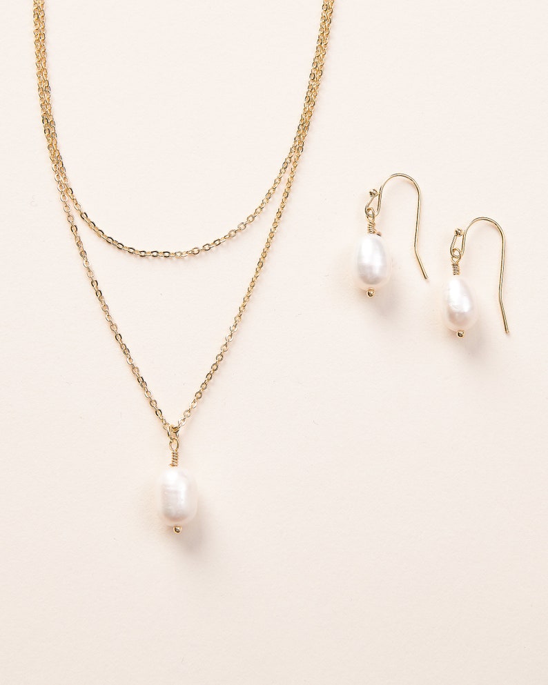 Pu&ograve; includere: Una collana a catena dorata con un ciondolo a perla singola e orecchini a goccia di perla abbinati. La collana &egrave; composta da due catene sovrapposte.