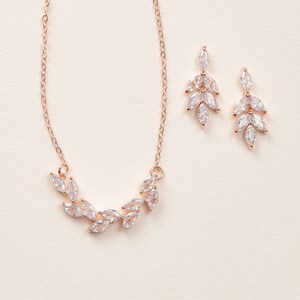 May include: A rose gold necklace and earrings set with a delicate leaf design featuring clear cubic zirconia stones.