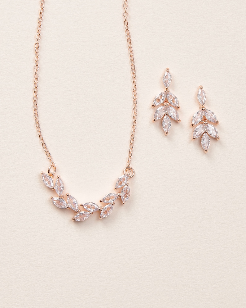 May include: A rose gold necklace and earrings set with a delicate leaf design featuring clear cubic zirconia stones.
