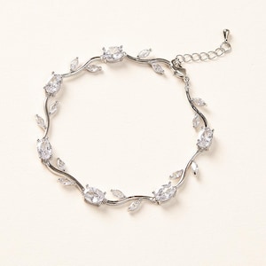 May include: A silver bracelet featuring a delicate vine design with oval-cut clear gemstones and small leaf accents. The adjustable chain allows for a comfortable fit. The bracelet is a piece of jewelry.