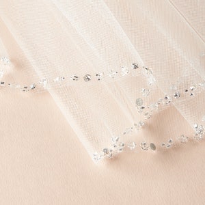 Op de afbeelding: Witte bruids sluier met een parelrand. De sluier is gemaakt van zacht tule en heeft een delicate, romantische uitstraling.