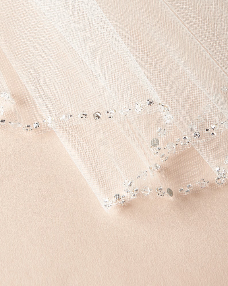 Op de afbeelding: Witte bruids sluier met een parelrand. De sluier is gemaakt van zacht tule en heeft een delicate, romantische uitstraling.