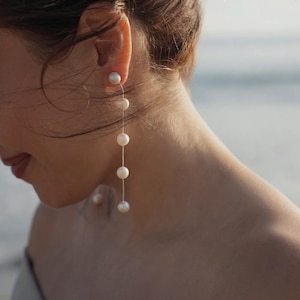 May include: A long, delicate pearl earring with a single pearl at the top and four pearls dangling below. The earring is silver in color and the pearls are white.