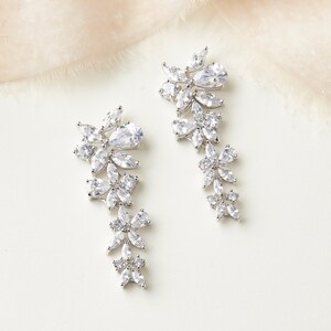 May include: A pair of silver dangle earrings with a floral design featuring clear cubic zirconia stones.