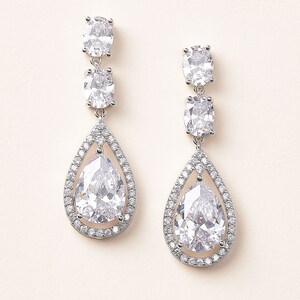 May include: A pair of silver dangle earrings with clear pear-shaped crystals surrounded by smaller crystals.