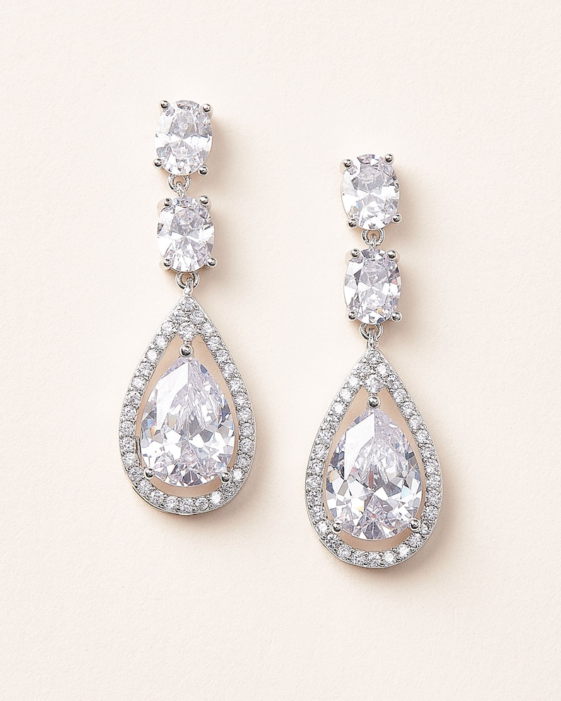 May include: A pair of silver dangle earrings with clear pear-shaped crystals surrounded by smaller crystals.