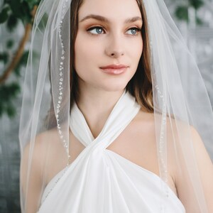 Op de afbeelding: Een witte bruids sluier met een delicate parelrand. De sluier is gemaakt van zacht tule en is perfect voor een eenvoudige en elegante bruiloft look.