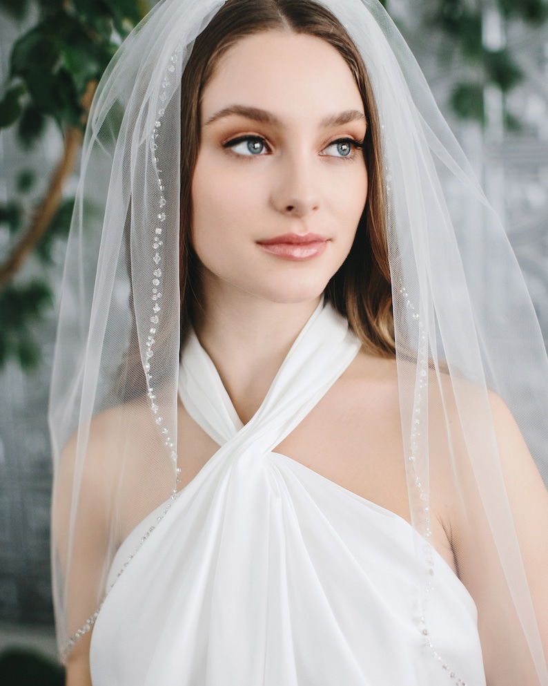 Op de afbeelding: Een witte bruids sluier met een delicate parelrand. De sluier is gemaakt van zacht tule en is perfect voor een eenvoudige en elegante bruiloft look.