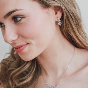 May include: A woman wearing a silver necklace and earrings with a leaf design. The necklace and earrings are made of small, clear stones.