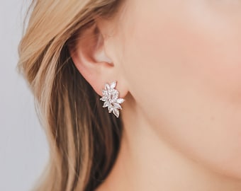 May include: A pair of silver earrings with a cluster of clear cubic zirconia stones in a floral design.