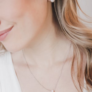 May include: A silver-toned necklace featuring a single white pearl pendant suspended from a delicate chain, accompanied by matching stud earrings. Each earring consists of a small clear stone set above a round white pearl, creating a coordinated set.