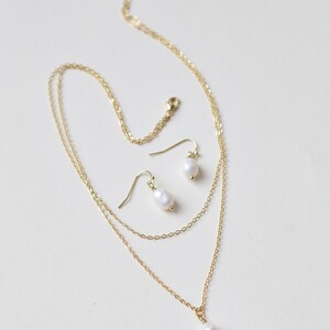 Pu&ograve; includere: Una collana a catena d'oro con due fili e un ciondolo di perla. Sono inclusi orecchini pendenti di perla abbinati.