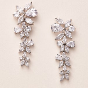 May include: A pair of silver dangle earrings with clear crystal stones arranged in a floral pattern.