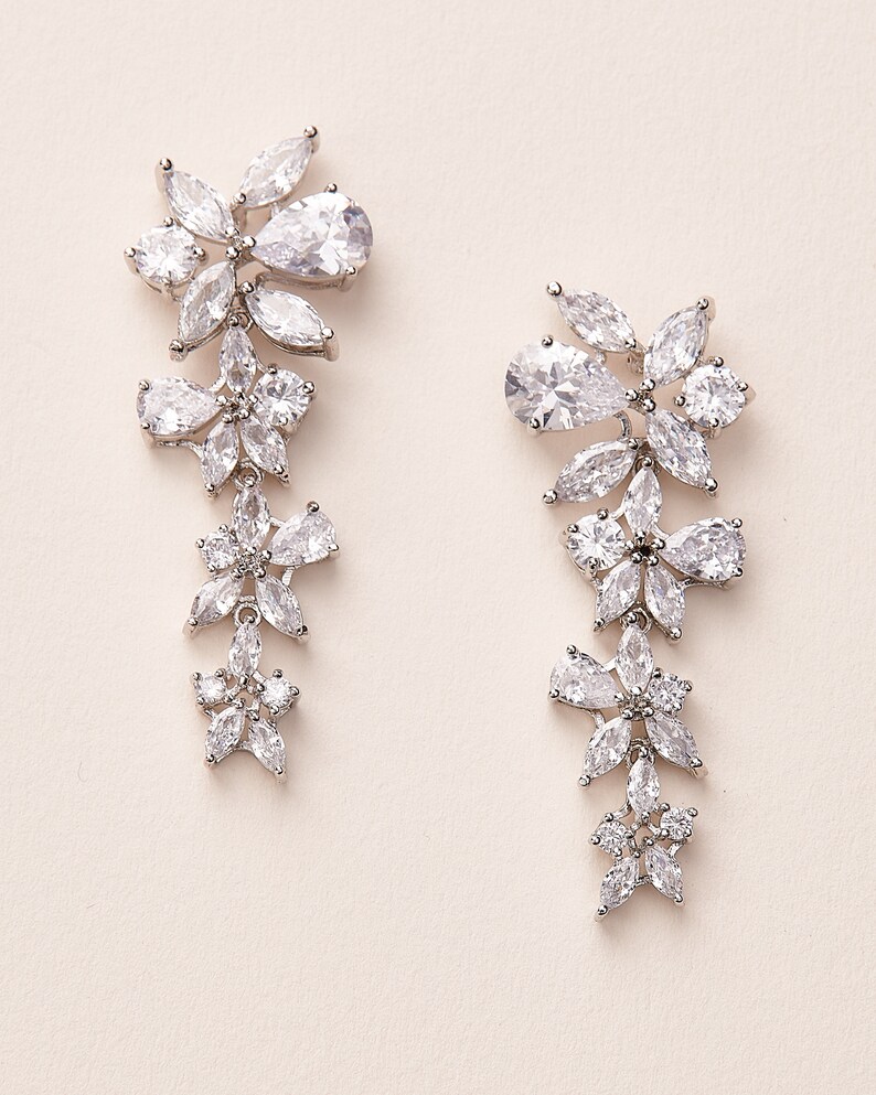 May include: A pair of silver dangle earrings with clear crystal stones arranged in a floral pattern.