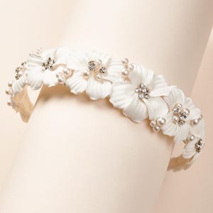 May include: White floral headband with pearl and rhinestone accents. The headband is made of fabric flowers and is perfect for a wedding or special occasion.