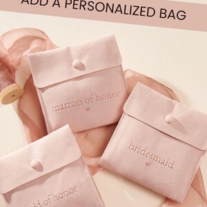 May include: Three square, light pink velvet pouches with snap closures. Each pouch features embroidered text: matron of honour, bridesmaid, and maid of honour, each with a small heart icon. The text ADD A PERSONALIZED BAG appears at the top.