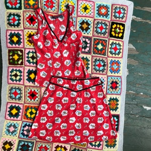 Peut inclure: Un haut sans manches rouge et blanc et une jupe assortie avec une bordure noire. Le haut a un col en V et la jupe a une taille haute. Le tissu a un motif de petits avions rouges.